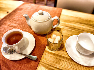 A cozy afternoon tea setting with a teapot, cup, sugar cubes, and an empty saucer on a wooden table