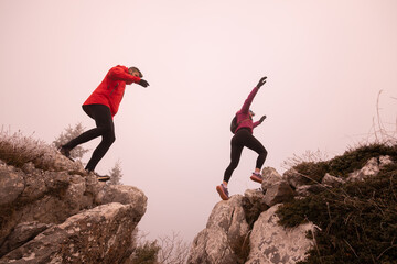  trail runner couple jumping over a cliff and running to a rocky mountain top in the early morning or night