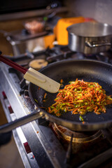Chef frying cut vegetables in pan in restaurant kitchen.