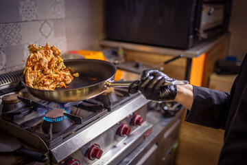 Chef frying cut vegetables and chicken in pan in restaurant kitchen.