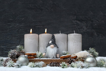 Zweiter Advent: Dekoration mit vier grauen Adventskerzen einem Wichtel und Weihnachtsschmuck im...