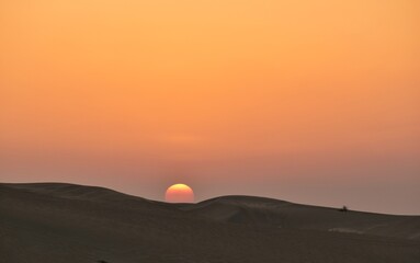 A Scenic picture of the sun setting against the sand dunes.