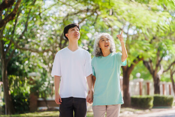 Obraz premium Young son and his mature mom asian people share loving hug in beautiful park, surrounded by nature. Their happiness radiates as they bond outdoors, celebrating family love and togetherness.