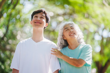 Obraz premium Young son and his mature mom asian people share loving hug in beautiful park, surrounded by nature. Their happiness radiates as they bond outdoors, celebrating family love and togetherness.