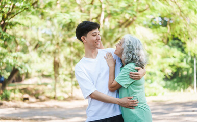 Fototapeta premium Young son and his mature mom asian people share loving hug in beautiful park, surrounded by nature. Their happiness radiates as they bond outdoors, celebrating family love and togetherness.