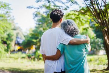 Young son and his mature mom asian people share loving hug in beautiful park, surrounded by nature. Their happiness radiates as they bond outdoors, celebrating family love and togetherness.