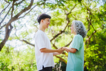 Obraz premium Young son and his mature mom asian people share loving hug in beautiful park, surrounded by nature. Their happiness radiates as they bond outdoors, celebrating family love and togetherness.