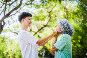 Young son and his mature mom asian people share loving hug in beautiful park, surrounded by nature. Their happiness radiates as they bond outdoors, celebrating family love and togetherness.