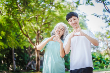 Young son and his mature mom asian people share loving hug in beautiful park, surrounded by nature. Their happiness radiates as they bond outdoors, celebrating family love and togetherness.