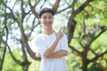 young man Asian people enjoys a moment of relaxation in a serene park, surrounded by trees and nature. His happiness and self-love shine through as he embraces the peaceful outdoors.