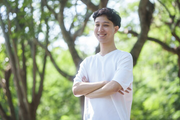 young man Asian people enjoys a moment of relaxation in a serene park, surrounded by trees and nature. His happiness and self-love shine through as he embraces the peaceful outdoors.