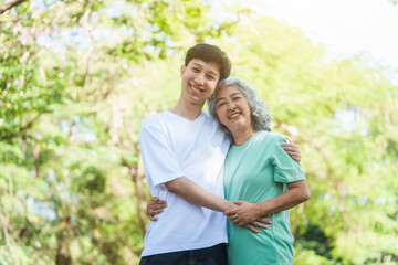 Young son and his mature mom asian people share loving hug in beautiful park, surrounded by nature. Their happiness radiates as they bond outdoors, celebrating family love and togetherness.