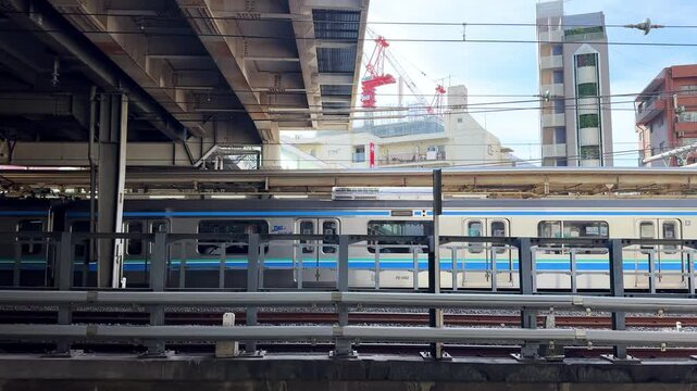 Urban train passing under an overpass at a bustling Tokyo station on a sunny day