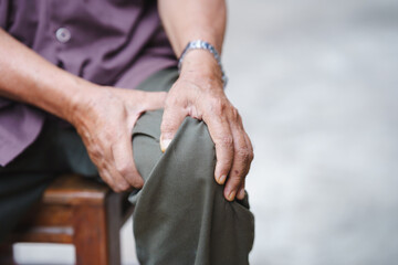 person holding their knee, showing signs of discomfort or pain, possibly indicating health issue. focus is on hands and knee area, conveying sense of struggle