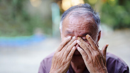 An elderly man expresses deep emotion, covering his face with his hands, reflecting feelings of sadness or distress in natural outdoor setting