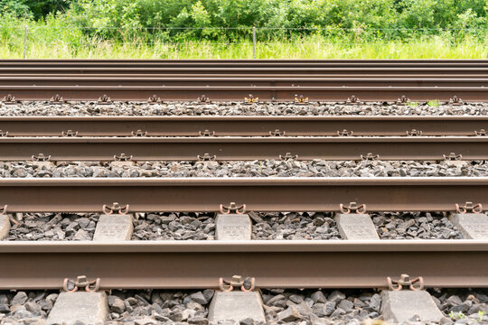 Pattern of five railway tracks on gravel as a side view. Fence runnimg parallel to the tracks and green landscape with grass and bushes in the background.