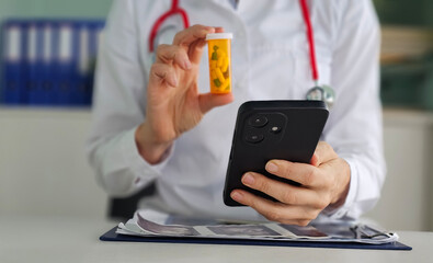 Doctor holding prescription bottle while using smartphone in office during patient consultation concept