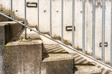 Stairs with metal handrail and concrete wall with lights in the background. Stairs and wall are already mossy and weathered.