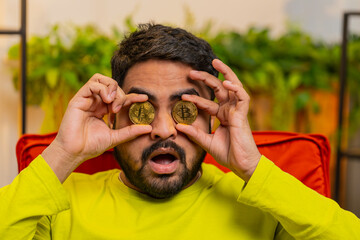 Indian man freelancer holding two gold coins, successful developer programmer. Guy stock trader...