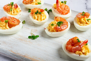 Boiled eggs stuffed with yolk and seasoned with mayonnaise, stuffed eggs with shrimp, on a white wooden chopping board, selective focus, close-up, without people,