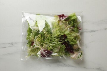 Pack of fresh salad mix on white marble table, top view