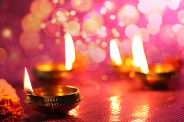 Diwali celebration. Diya lamps and beautiful flowers on color background, closeup. Space for text. Bokeh effect
