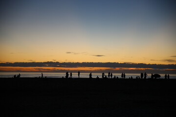 Beautiful sunset over the sea with vibrant colors reflecting on the water. Silhouettes of unrecognizable people on the beach create a peaceful, serene scene perfect for travel and nature themes