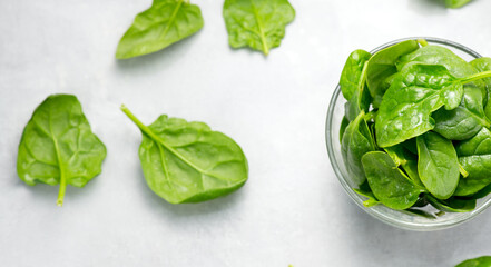 Spinach leaves in a transparent glass bowl on light gray table background. Heap of Baby spinach fresh leaves close up, border design. Healthy vegan food, diet, dieting. Top view. 