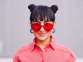 Latin america woman whit love heart red shape sunglasses and buns hairstyle, front portrait. Pink clothes. Valentine's day, 14 february love, friendship and emotion concept. hispanic brunette  ecuador