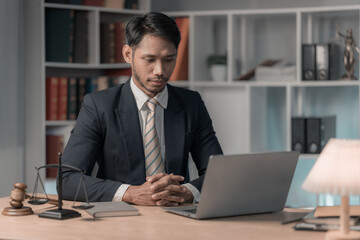Obraz premium Lawyer working or reading law book working with laptop in office as legal counsel, justice and law. Male judge in courtroom on wooden table.