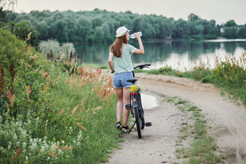 A girl cyclist drinks water from a bottle while cycling in the park.
