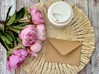 White cup of coffee, brown envelope and fresh pink peonies