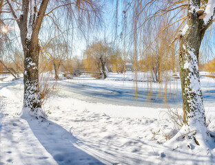 Fabulous landscape in city park with snowy trees and beautiful frozen river and footbridge