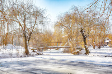 Obraz premium Fabulous landscape in city park with snowy trees and beautiful frozen river and footbridge