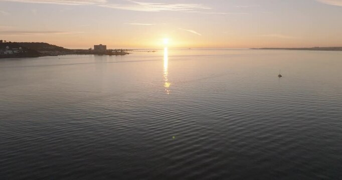Aerial drone shot of the Tagus river, Atlantic Ocean and horizon at sunset in Lisbon, Portugal, Europe. Catamaran facing the sun. Forte do Bugio lighthouse visible. Shot in ProRes 422 HQ