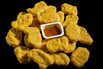 A tray of golden colored chicken nuggets sits on a black background. The tray is filled with...