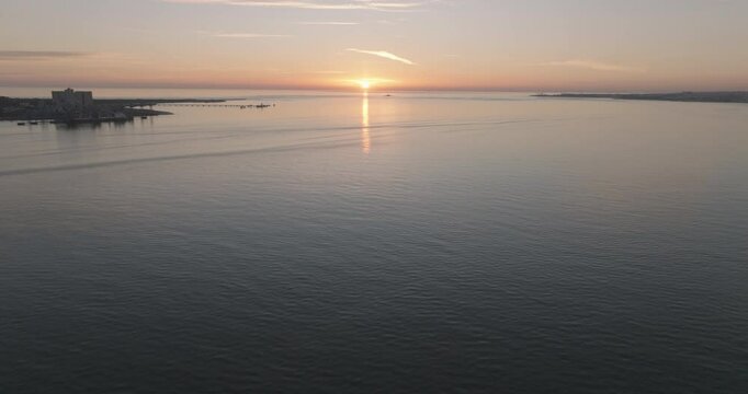 Aerial drone shot of the Tagus river, Atlantic Ocean and horizon at sunset in Lisbon, Portugal, Europe. Catamaran facing the sun. Forte do Bugio lighthouse visible. Shot in ProRes 422 HQ