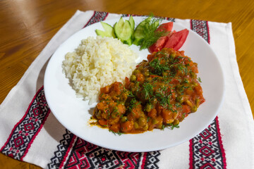 Boiled rice with stewed and fresh vegetables on white dish