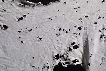 Ripped white fabric with many holes, ragged cloth with holes, grunge damaged white shirt on black...