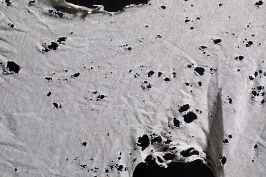 Ripped white fabric with many holes, ragged cloth with holes, grunge damaged white shirt on black background