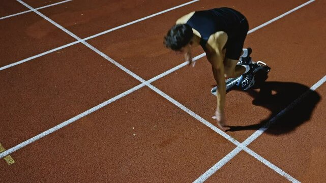 Strong Young Man Starting a Race From Track Starting Blocks Position on a Dark Stadium in the Evening. Cinematic Portrait of a Fit Male Sprint Runner Participating in a Competition
