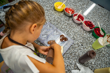 Little girl learning how to cook in a cooking class. Handmade dessert. Making chocolate candy, Child filling heart shaped mold with chocolate