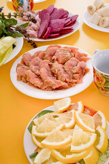 Salted red fish, sausage, sliced lemon and other products lie on a plate on a served table.