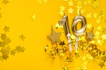 Gold candle in shape of number ten on yellow background surrounded by stars confetti and streamers.