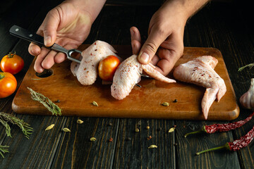Hands meticulously arrange chicken wings and ripe tomatoes on a wooden cutting board. Aromatic...