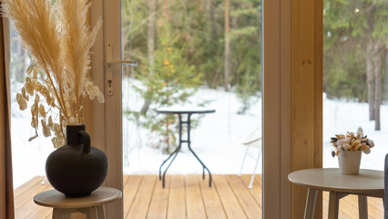 View from house to forest and recreation area on winter day. View from panoramic window. Tables with Scandinavian style decor. Isolated secluded vacation. Relaxation