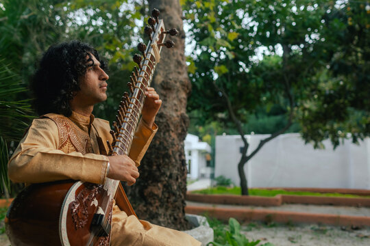 Indian musician in traditional clothes playing sitar festive season outdoor home. Happy Diwali greeting photo. Part of a series