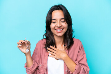 Young hispanic woman holding home keys isolated on blue background smiling a lot