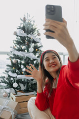 Happy red shirt Asian woman making a video call for holiday greeting with her friends and family showing the Christmas tree. . High quality photo