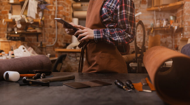 Concept technology in DIY tailor business. Leather craftsman uses computer tablet on atelier workshop